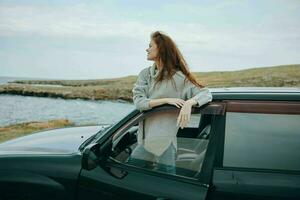 mulher com vermelho cabelo dentro uma suéter perto a carro natureza fêmea relaxante foto