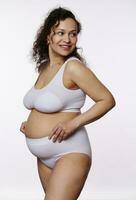 encantador grávida mulher posando nu barriga dentro lingerie branco fundo foto