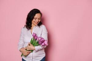 lindo jovem grávida mulher sentindo-me feliz, recebendo uma ramalhete do roxa tulipas. mãe dia e maternidade conceito foto