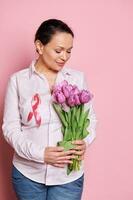 grávida mulher vestindo consciência fita, segurando ramalhete do roxa tulipas. Rosa Outubro - seio Câncer consciência mês foto