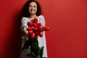 detalhes em ramalhete do vermelho tulipas dentro mãos do lindo sorridente mulher, vestido dentro ucraniano tradicional bordado vestir foto