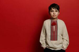 caucasiano adolescente Garoto vestindo linho camisa com bordado enfeite dentro ucraniano estilo, olhando às Câmera, isolado em vermelho foto