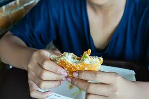 hamburguer dentro Rapazes mão, com fome Garoto segurando uma parcialmente mordido Hamburguer de queijo foto