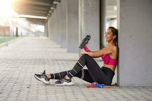 ginástica mulher relaxante depois de exercício com uma soro de leite proteína garrafa. relaxante depois de treinamento. lindo jovem mulher olhando longe enquanto em repouso depois de corrida foto