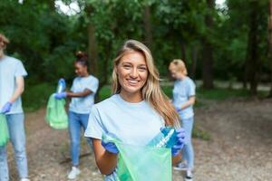 a jovem adulto mulher, quem é 1 do uma diverso grupo do voluntários, leva Tempo para sorrir para a Câmera. aguarde lixo saco e olhando às Câmera foto