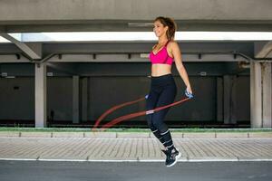 ginástica mulher saltando com uma saltar corda ao ar livre. fêmea fazendo ginástica Treinamento dentro manhã. Atlético lindo mulher exercícios com saltar saltando corda. foto