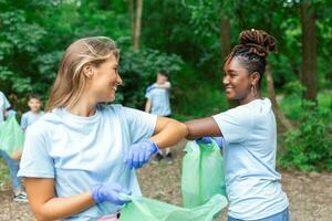 voluntário grupo limpeza parque a partir de bobagem. jovem mulher e homens caminhando através madeiras e carregando plástico bolsas. ao ar livre limpeza conceito foto