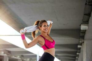 jovem atlética com toalha sorrindo e esticando. formação desportiva jovem. mulher fazendo exercícios de treino na rua. garota em forma se alongando antes do treinamento físico ativo foto