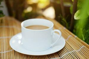 mão segurando branco cerâmico copo do quente café em tecido esteira com natural luz manhã dentro a jardim. cafeína bebidas causa uma fresco sentimento. foto