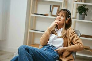 sonhando feliz jovem Loiras senhora dentro caloroso suéter dentro fones de ouvido parece a parte, de lado ouço fav canções sentado dentro poltrona às moderno casa interior. música Tempo relaxante legal lista de reprodução conceito. cópia de espaço foto