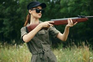 mulher soldado Caçando é segurando Sombrio visando óculos dentro frente do ele com uma arma de fogo armas foto