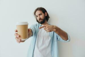 freelance milenar homem com uma barba bebendo café a partir de uma reciclado copo dentro à moda hipster roupas branco camiseta azul jeans e camisa em uma branco fundo foto