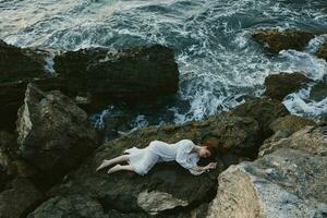 lindo mulher dentro uma isolado local em uma selvagem rochoso costa dentro uma branco vestir período de férias conceito foto