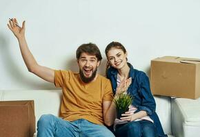 alegre jovem casal dentro a quarto em a sofá com caixas comovente foto
