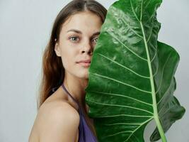 bonita mulher dentro roupa de banho segurando grande verde folha perto face isolado fundo foto