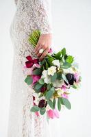 menina alegre noiva em um vestido de malha branco posando com um buquê de flores foto