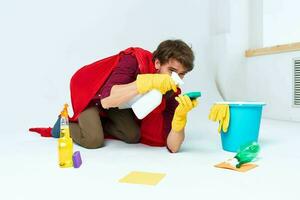 uma homem com limpeza suprimentos dentro uma vermelho capa de chuva em a chão do uma casa interior profissional foto