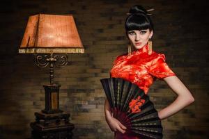 garota em um vestido de seda japonesa vermelha qipao em um quarto escuro foto