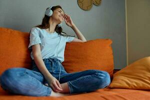 mulher sentado em a sofá às casa ouvindo para música em fones de ouvido estilo de vida foto