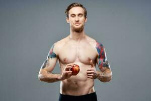 jovem homem com maçã e bombeado acima tronco bíceps homem tatuagem cinzento fundo cortada Visão foto