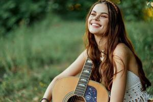 hippie mulher sorridente e abraçando dela guitarra dentro natureza dentro a parque dentro a pôr do sol luz foto