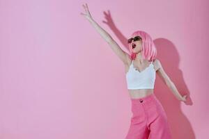 lindo elegante menina dentro Rosa calça oculos de sol posando Rosa fundo inalterado foto