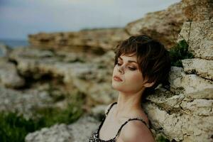 elegante mulher curto corte de cabelo posando sentado em a pedras estilo de vida foto