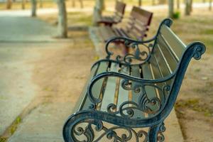 close-up de um banco de aço enferrujado com bancos de madeira borrados ao fundo em um parque público ao ar livre foto