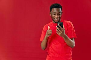 bonita homem do africano aparência em uma vermelho fundo e tela sensível ao toque telefone cópia de espaço foto