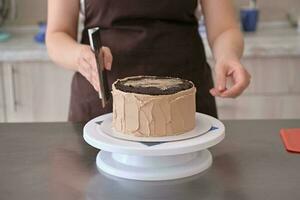 mulher pastelaria chefe de cozinha linhas chocolate creme em chocolate bolo, fechar-se. bolo fazer processo, seletivo foco foto