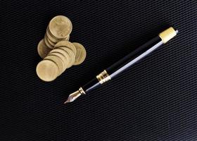 caneta-tinteiro e pilha de moedas no fundo de couro para o conceito de negócio foto