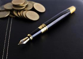 caneta-tinteiro e pilha de moedas no livro de couro para o conceito de finanças empresariais foto