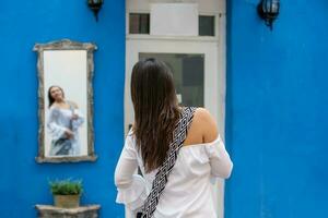 lindo mulher em branco vestir olhando às ela mesma em uma espelho em a colorida ruas do a colonial murado cidade do cartagena de índias foto