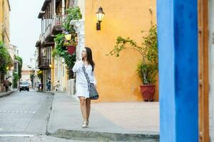 lindo mulher em branco vestir caminhando sozinho às a colorida ruas do a colonial murado cidade do cartagena de índias foto