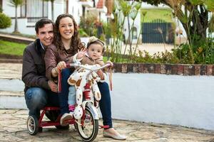 1 ano velho bebê ao ar livre equitação dela triciclo com dela pais. foto