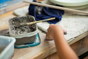 movimento borrou as mãos de uma garota moldando um trabalho de argila com lama úmida em uma bandeja de plástico foto