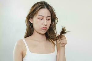 estragado cabelo, frustrado ásia jovem mulher, menina mão dentro segurando divisão termina, bagunçado não escovado seco cabelo com face choque, grandes desgrenhado cabelo, saúde Cuidado do beleza. retrato isolado em fundo. foto