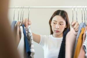 escolha do roupas, nada para vestir. atraente ásia jovem mulher, menina experimentar em aparecer, feliz escolhendo vestir, equipamento em cabide dentro guarda roupa dentro quarto armário de roupa às lar. decidir blusa o que para colocar em que 1 foto