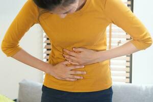 flatulência ásia jovem mulher, menina mão dentro estômago dor, Sofra a partir de Comida envenenamento, abdominal dor e cólon problema, gastrite ou diarréia. paciente barriga, abdômen ou inflamação, conceito. foto