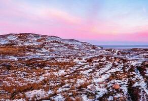 surpreendente nascer do sol polar panorama com uma branco neve cume do montanhas atrás a rochoso montanhas e uma penhasco. Maravilhoso panorâmico montanha panorama com tundra. foto