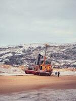 a velho oxidado pescaria barco abandonado de uma tempestade em a costa. cemitério do navios, velho pescaria Vila em a costa do a barents mar foto