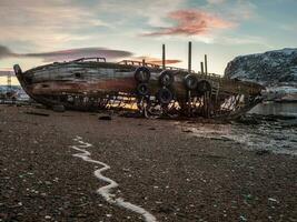 a velho oxidado pescaria barco abandonado de uma tempestade em a costa. cemitério do navios, velho pescaria Vila em a costa do a barents mar, a cola Península, teriberka foto