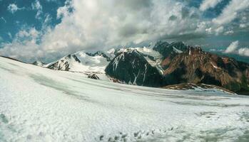 Nevado montanha declive. panorâmico alpino panorama com coberto de neve montanha pico e afiado pedras debaixo dramático céu. colorida ensolarado montanha cenário com neve montanha topo. foto