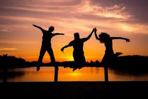 silhueta retrato grupo de pessoas pulando com a luz do pôr do sol no fundo foto