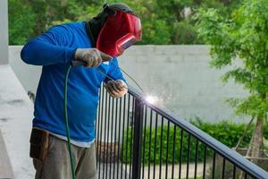 closeup retrato de soldador com máscara soldando a estrutura de aço da cerca preta com faíscas de luz e fumaça foto