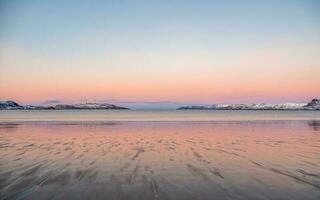 lindo Rosa pôr do sol em a ártico oceano. uma Península com coberto de neve colinas em a horizonte. mar minimalista panorama. foto