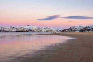 uma grupo do Viajantes dentro a distância em a de praia. lindo Rosa pôr do sol em a ártico oceano. uma Península com coberto de neve colinas em a horizonte. mar minimalista panorama. foto