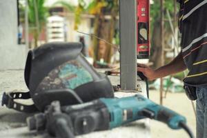 trabalhador mede o nível perpendicular durante a instalação do poste de aço no canteiro de obras pela régua de nivelamento com ferramentas borradas em primeiro plano foto