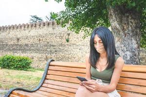 mulher com uma máscara sentada em um banco do parque foto