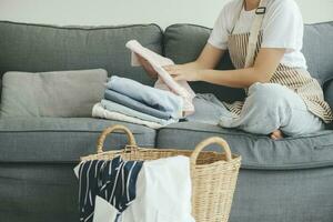 jovem mulher dobrando roupas em sofá às lar. foto